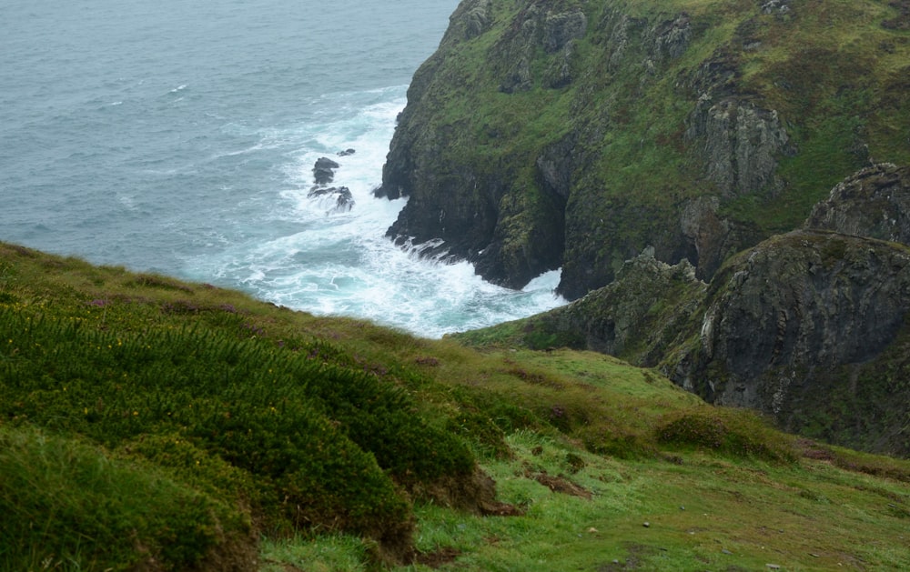 green grass covered mountain beside sea during daytime