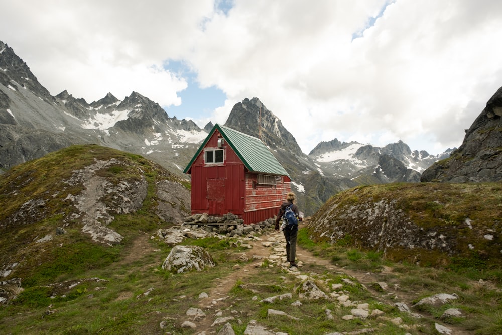 person in red jacket walking on green grass field near red wooden house during daytime