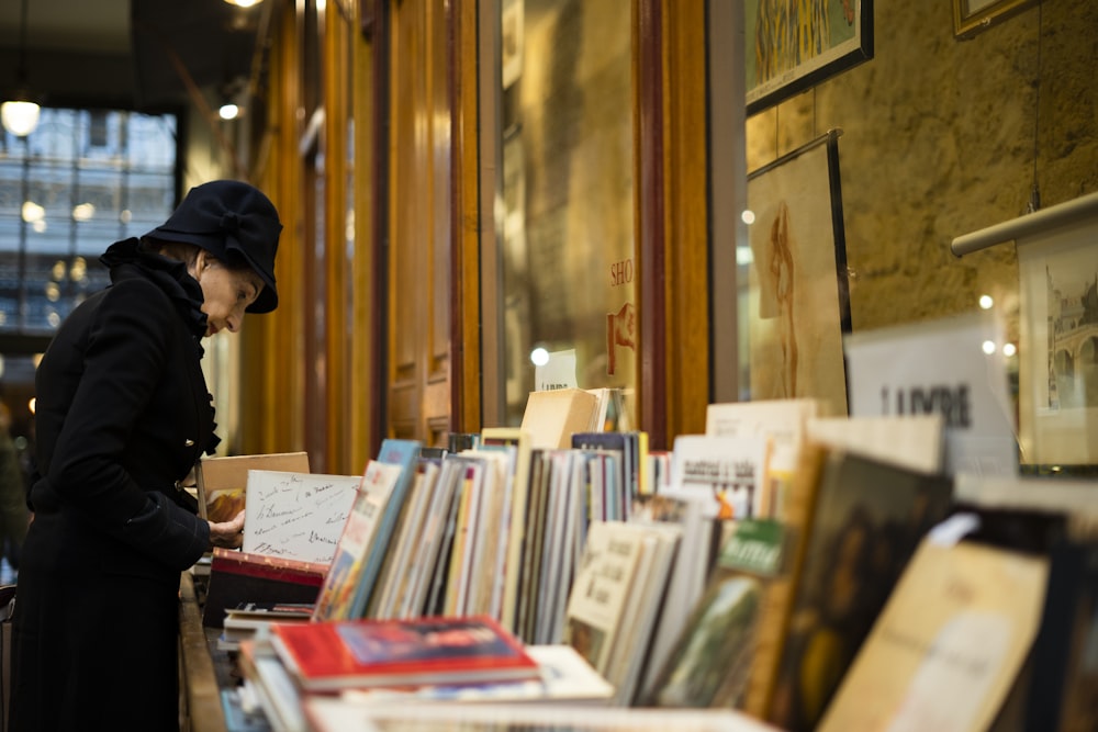 man in black cap standing in front of books