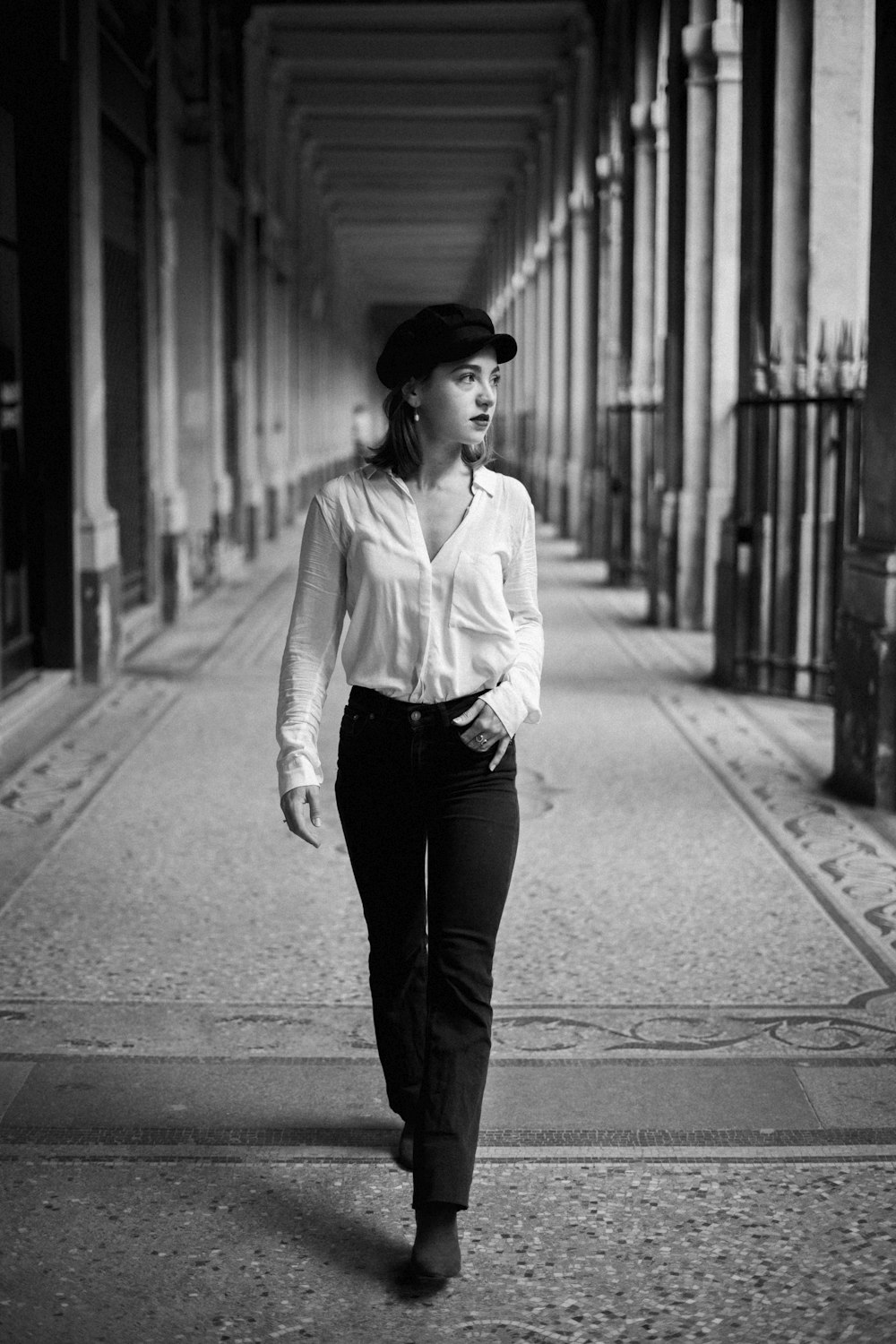 grayscale photo of woman in white long sleeve shirt and black pants standing on sidewalk