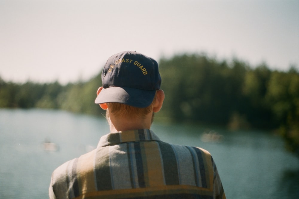 man in black and yellow stripe shirt wearing black cap standing near lake during daytime