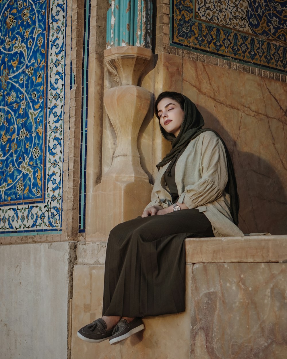 femme en hijab noir assise sur un banc en béton brun