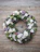 A serene funeral wreath arrangement with soft white flowers and dark green leaves on a wooden table.