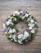 A serene funeral wreath with white lilies and green foliage placed gently on a wooden table.