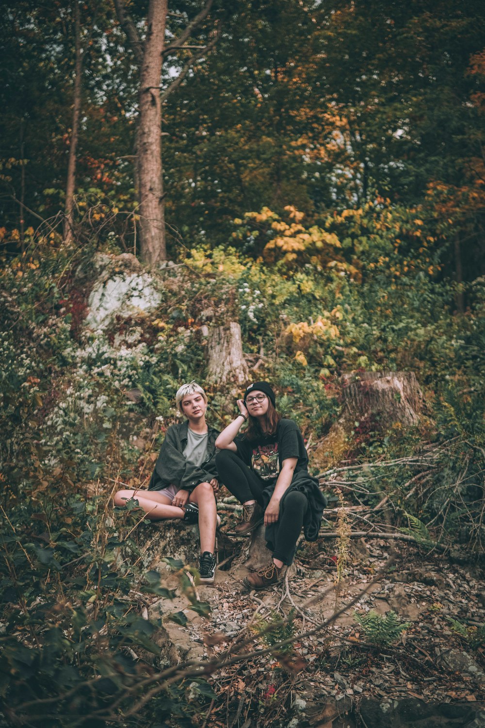 man and woman sitting on ground surrounded by trees during daytime