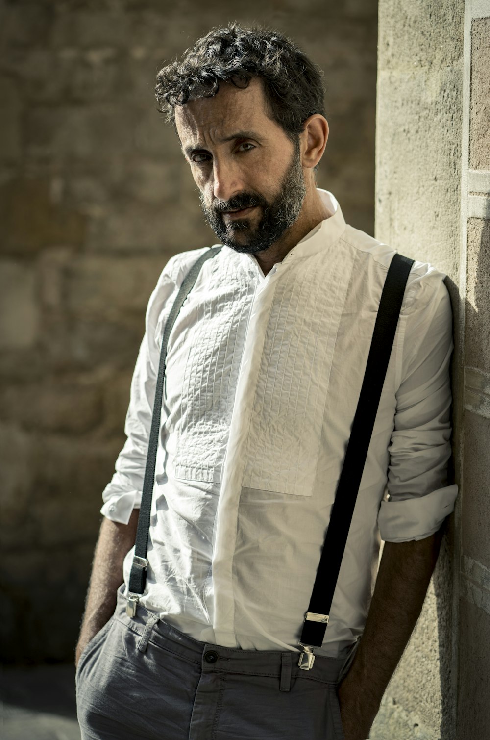 man in white dress shirt and black backpack standing beside brown concrete wall during daytime