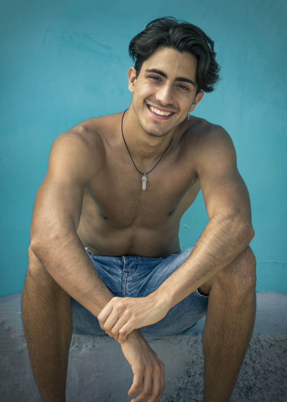 topless man in blue shorts sitting on brown concrete floor