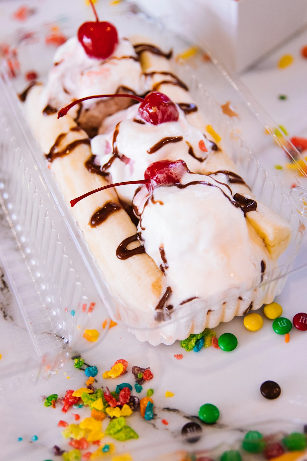 white cake with red and yellow sprinkles on clear plastic container