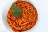 A white bowl filled with chunky tomato-based sauce, garnished with two green bay leaves on top.