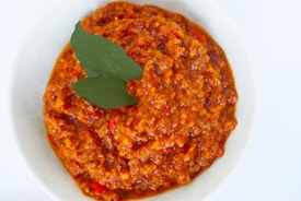 A white bowl filled with chunky tomato-based sauce, garnished with two green bay leaves on top.