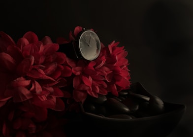 A trio of watches in black, white, and pink resting on a wooden table beside a delicate flower.