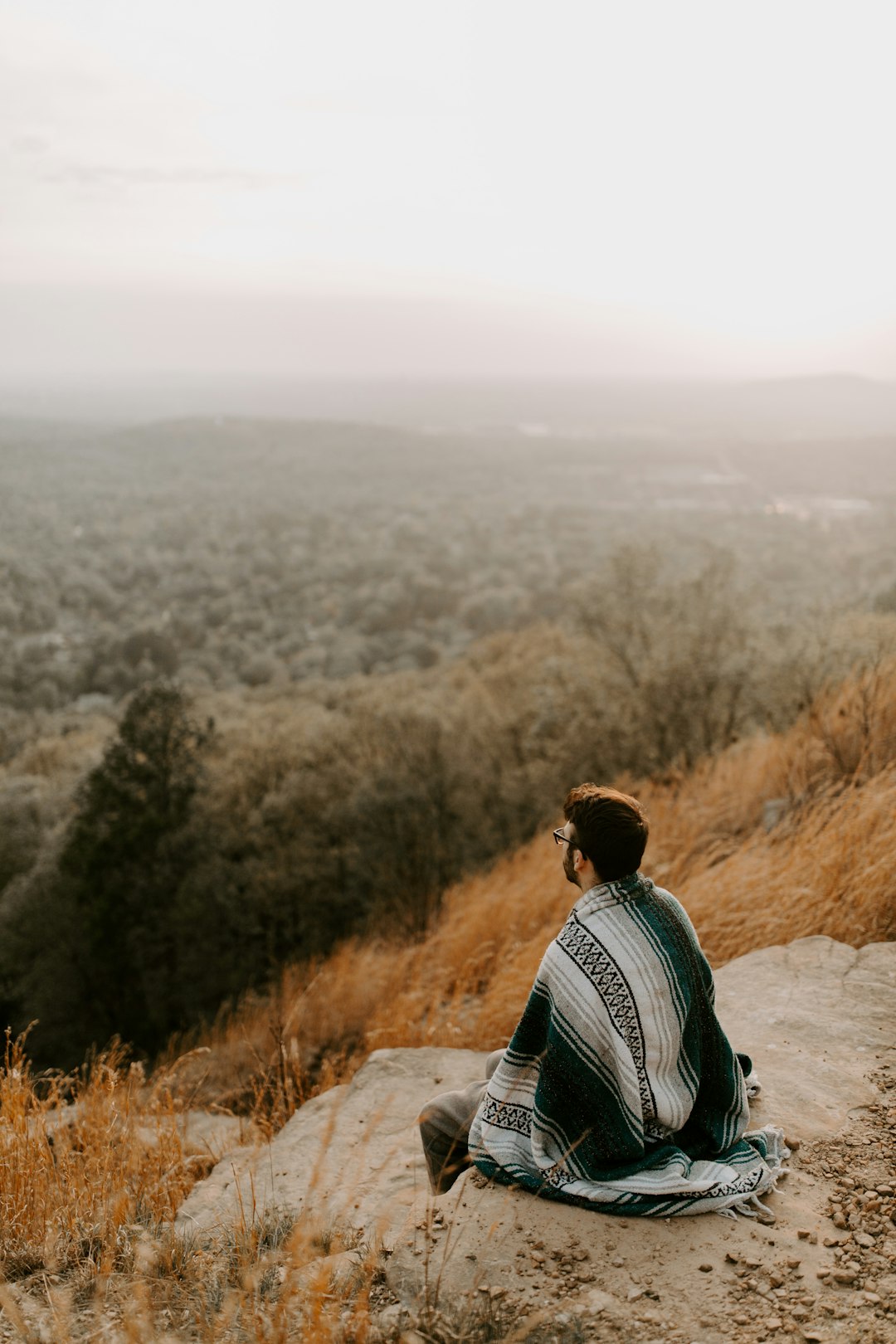 man in black and white striped shirt sitting on brown rock during daytime