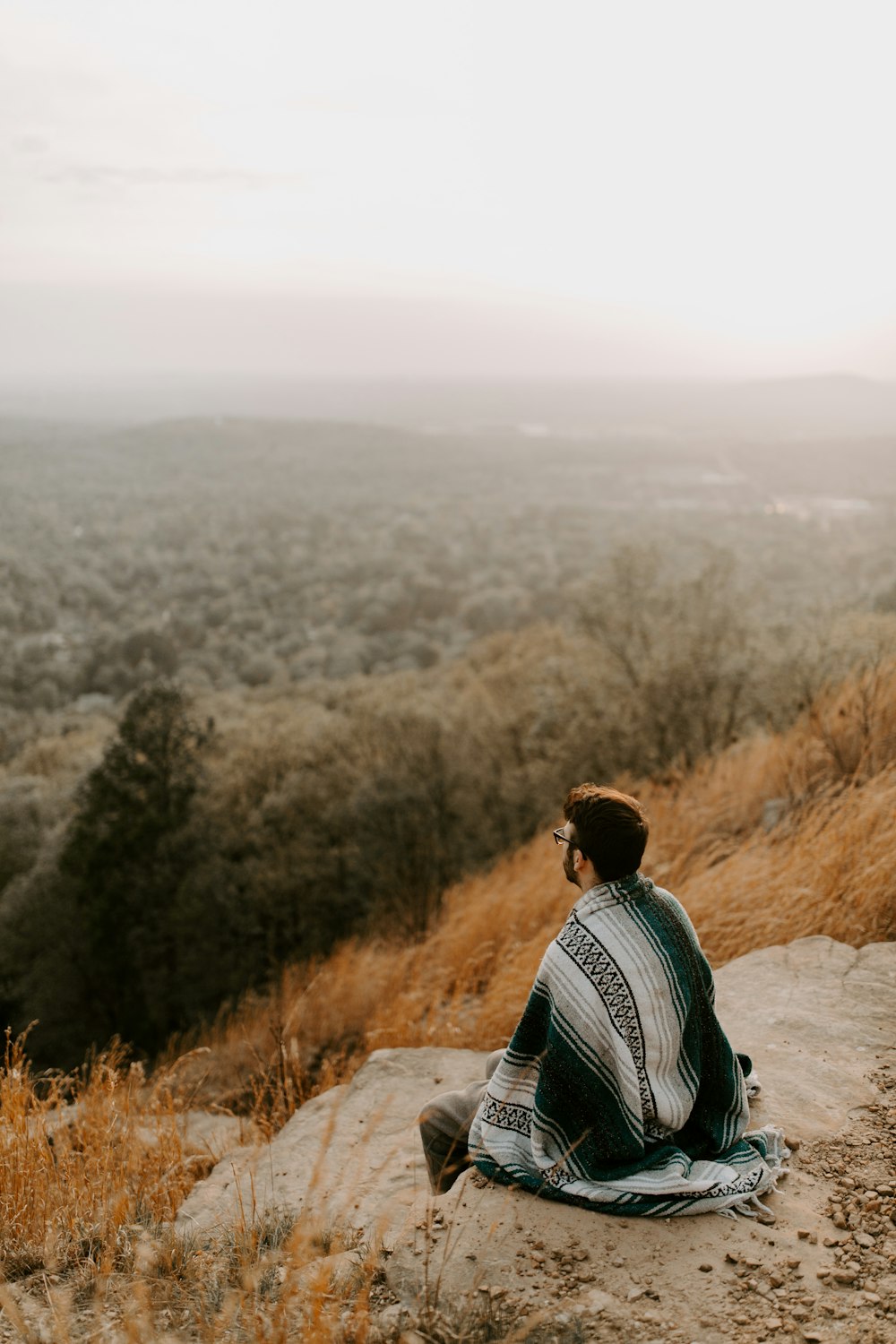 man in black and white striped shirt sitting on brown rock during daytime