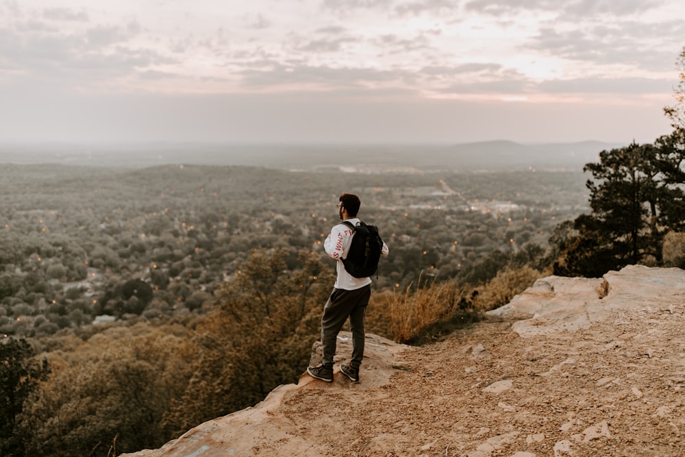 man in white shirt and black pants standing on brown rocky mountain during daytime