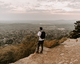 man in white shirt and black pants standing on brown rocky mountain during daytime