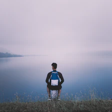 A serene mountain lake at sunrise with a lone backpacker sitting on a rock, enjoying the view.