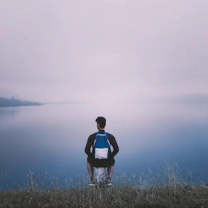 A serene mountain lake at sunrise with a lone backpacker sitting on a rock, enjoying the view.