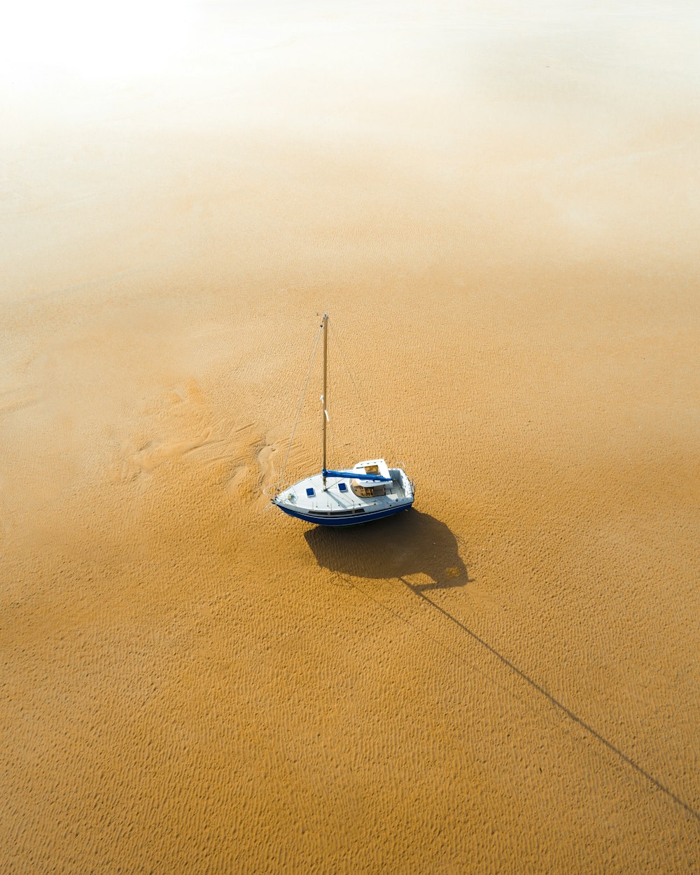 weißes und blaues Boot auf braunem Sand tagsüber