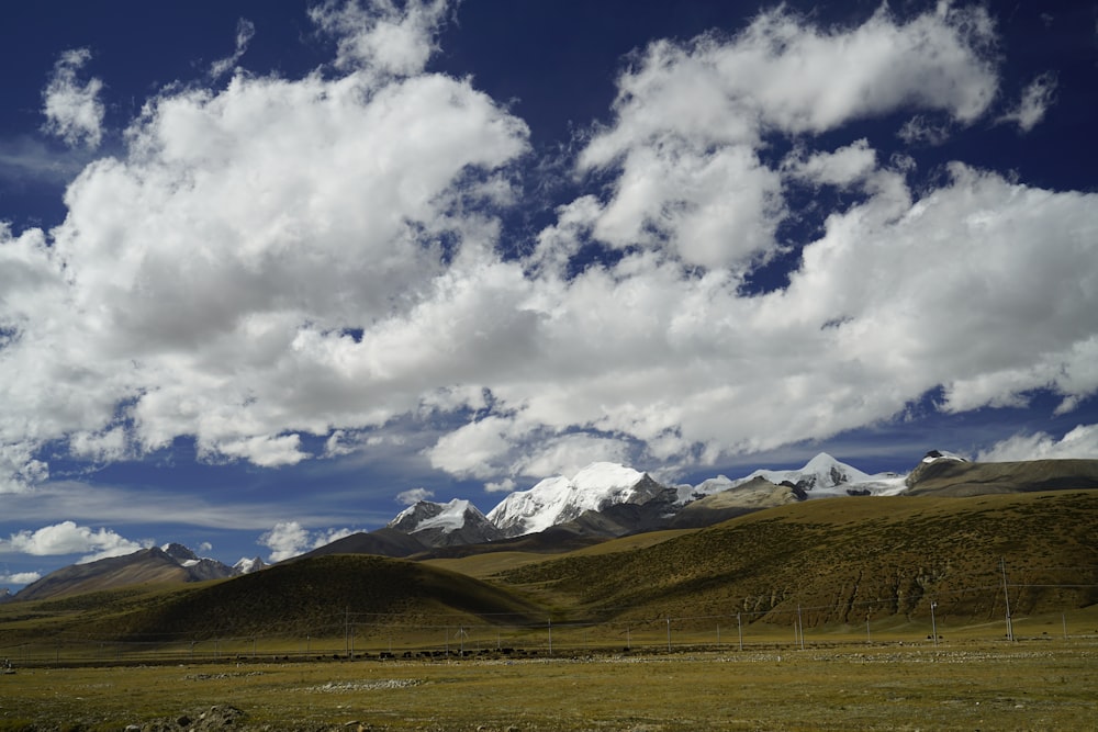 green grass field and mountains under white clouds and blue sky during daytime