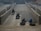 A brick kiln where several workers are molding clay into bricks. Rows of stacked bricks line the sides, and a dirt pathway runs through the middle. Workers are engaged in labor-intensive tasks, with one pushing a wheelbarrow filled with materials.