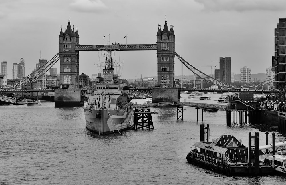 grayscale photo of people on boat on river near bridge