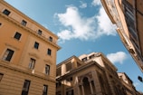 Traditional European-style buildings with multiple windows and ornate architectural details under a bright blue sky with scattered white clouds.