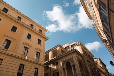Traditional European-style buildings with multiple windows and ornate architectural details under a bright blue sky with scattered white clouds.