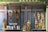 A storefront display featuring various golden religious statues and decorative items. The display includes figures of Christian saints and the crucifix, with intricate gold detailing. Floral arrangements in vases and plaques are also part of the presentation.