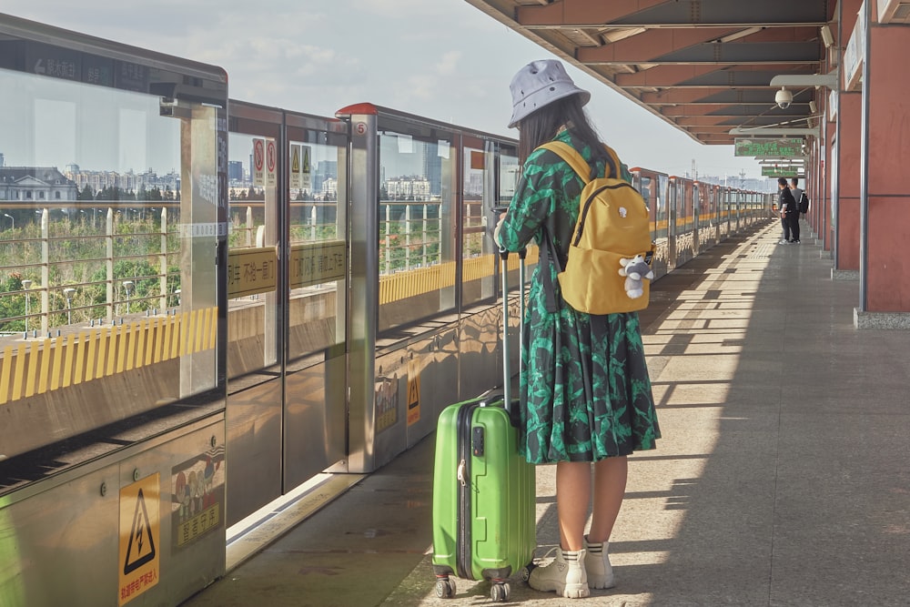 Mujer con vestido verde y azul de pie al lado del tren durante el día