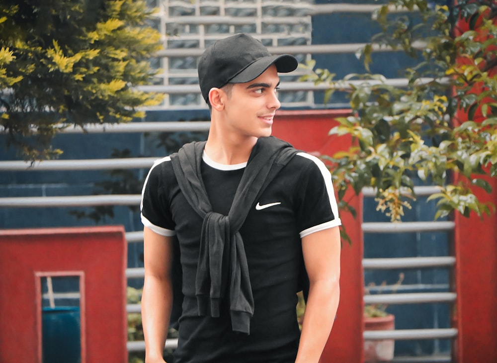 boy in black and white crew neck t-shirt and black cap standing near green tree