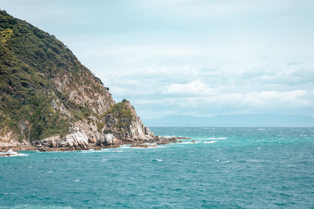 formazione rocciosa verde e marrone sul mare sotto il cielo blu durante il giorno