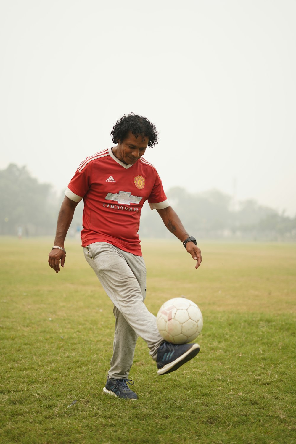 昼間、緑の芝生のグラウンドでサッカーボールを蹴る赤と白のサッカージャージを着た男性