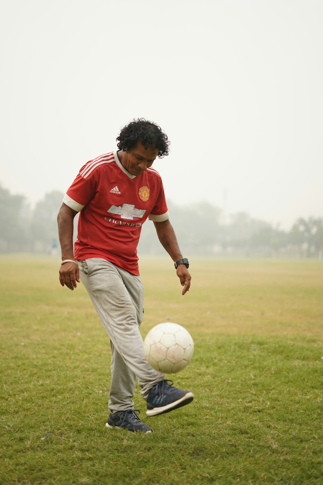 man in red and white soccer jersey kicking soccer ball on green grass field during daytime