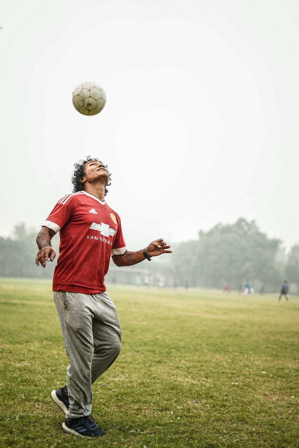 man in red and white soccer jersey shirt and gray pants standing on green grass field