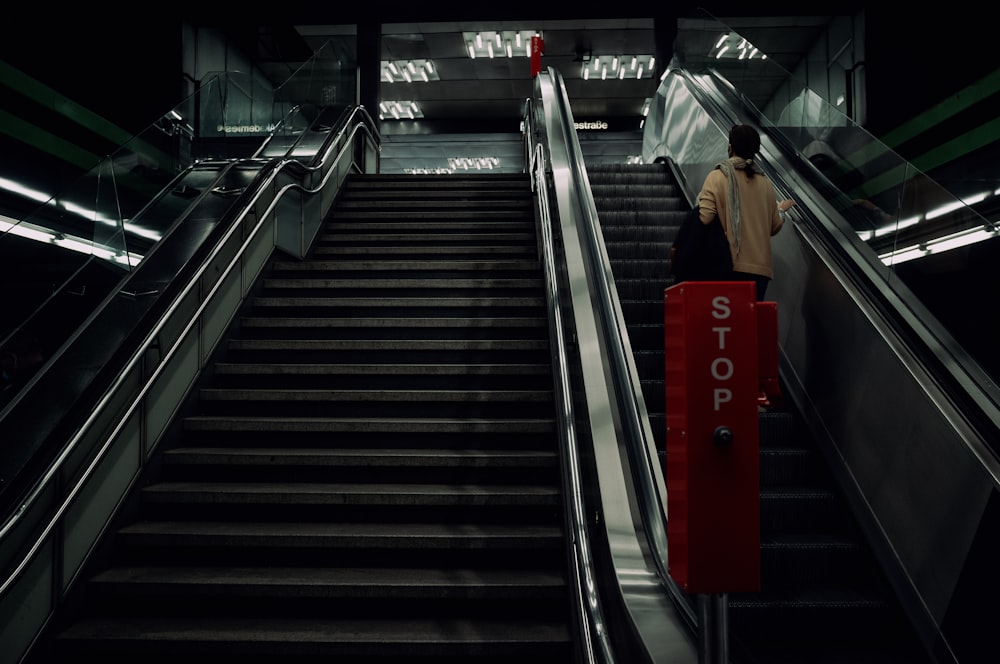 Mujer con vestido rojo caminando por la escalera mecánica negra y gris