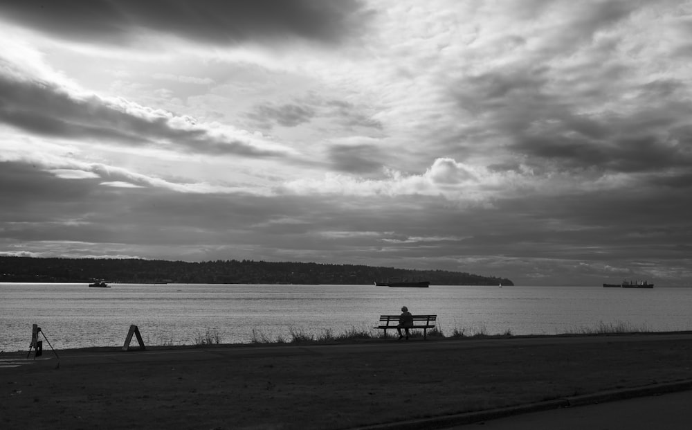 a black and white photo of a bench and a body of water