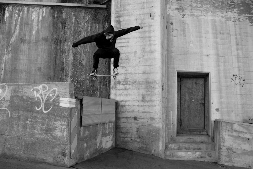 man in black jacket and pants jumping on mid air near concrete wall during daytime