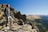 Traveler standing on a rocky ridge overlooking the vast Spiti Valley under a clear blue sky.