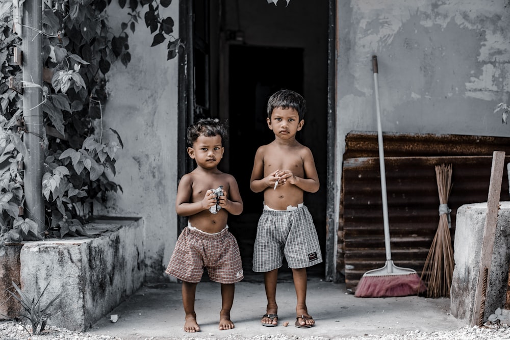 2 topless boys standing beside gray concrete wall