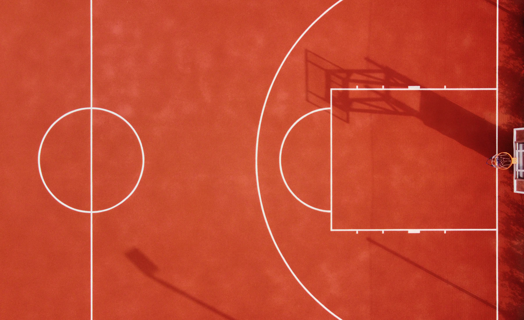 A red outdoor court from directly overhead, with the white key and center circle