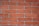 A close-up view of a red brick wall with visible mortar lines. The bricks are rectangular, arranged in a staggered pattern, and have a rough texture.