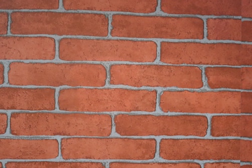 A close-up view of a red brick wall with visible mortar lines. The bricks are rectangular, arranged in a staggered pattern, and have a rough texture.