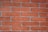 A close-up view of a red brick wall with visible mortar lines. The bricks are rectangular, arranged in a staggered pattern, and have a rough texture.