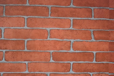 A close-up view of a red brick wall with visible mortar lines. The bricks are rectangular, arranged in a staggered pattern, and have a rough texture.