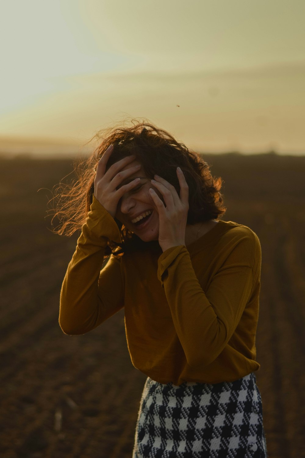 woman in brown long sleeve shirt covering her face with her hands