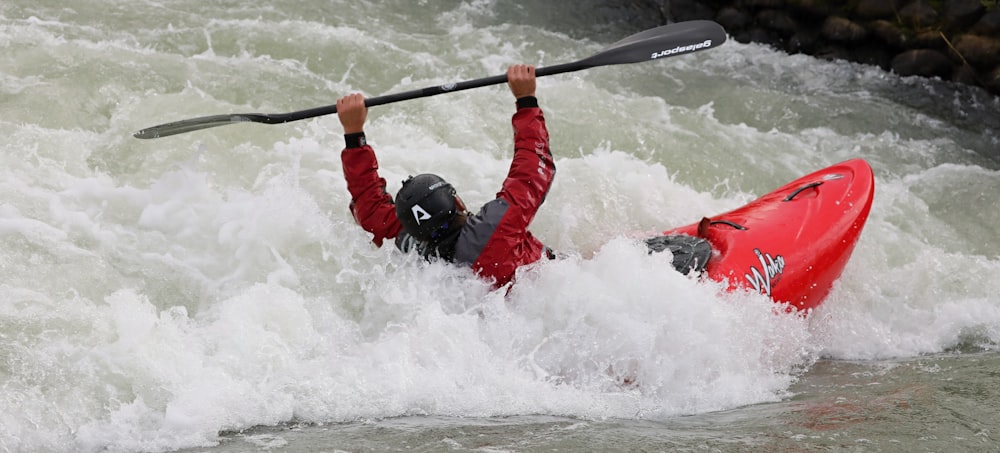 man in red jacket and black helmet riding red kayak on water during daytime