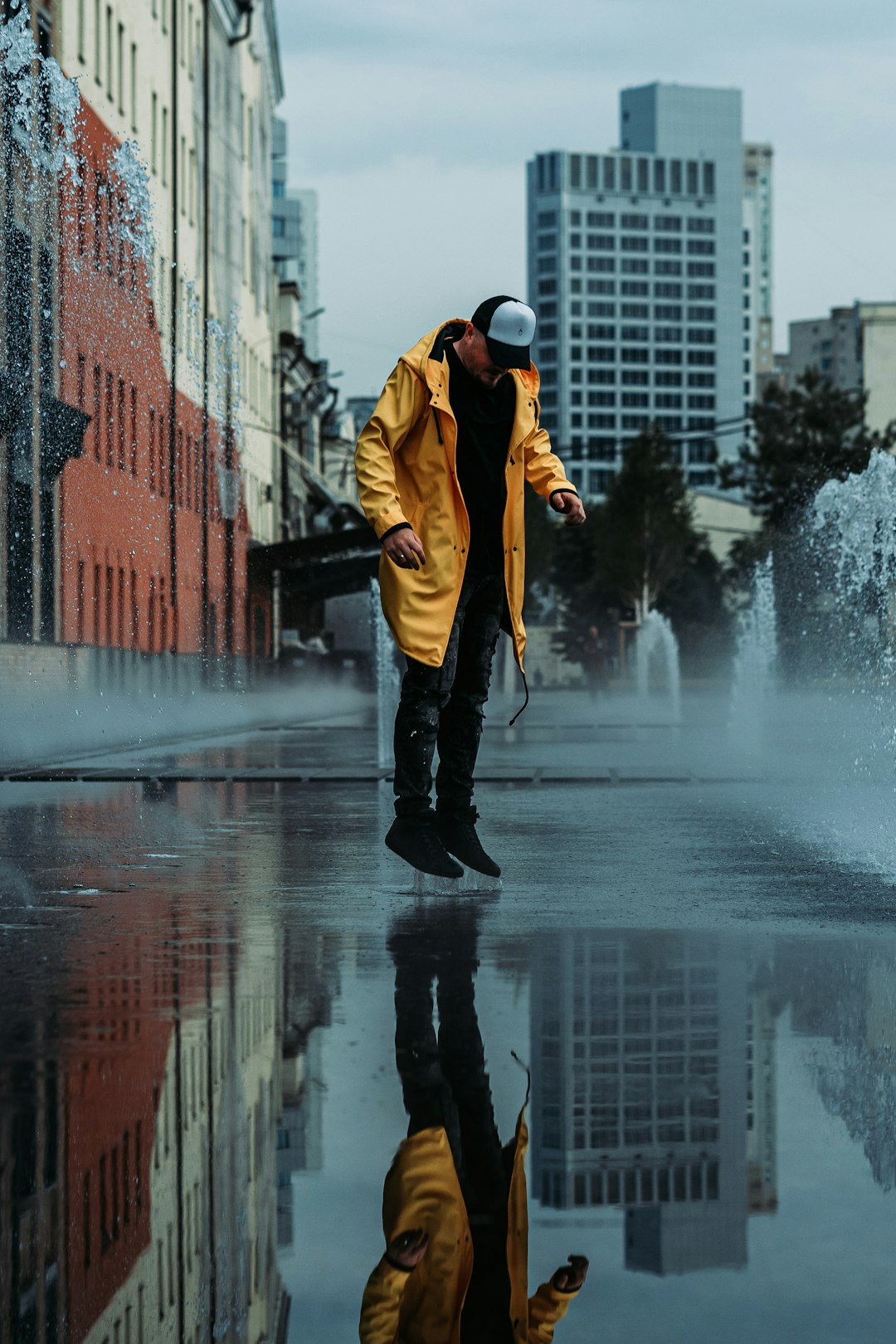 man in yellow jacket and black pants standing on wet road during daytime