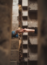 Two hands reaching towards each other between concrete walls, creating a sense of connection amidst a narrow, textured space.