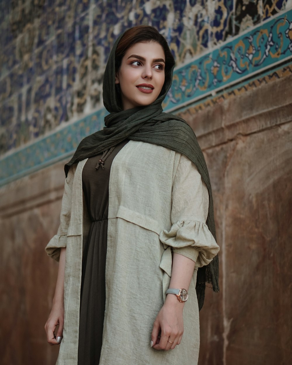 Frau im grauen Hijab steht tagsüber in der Nähe einer braunen Betonwand