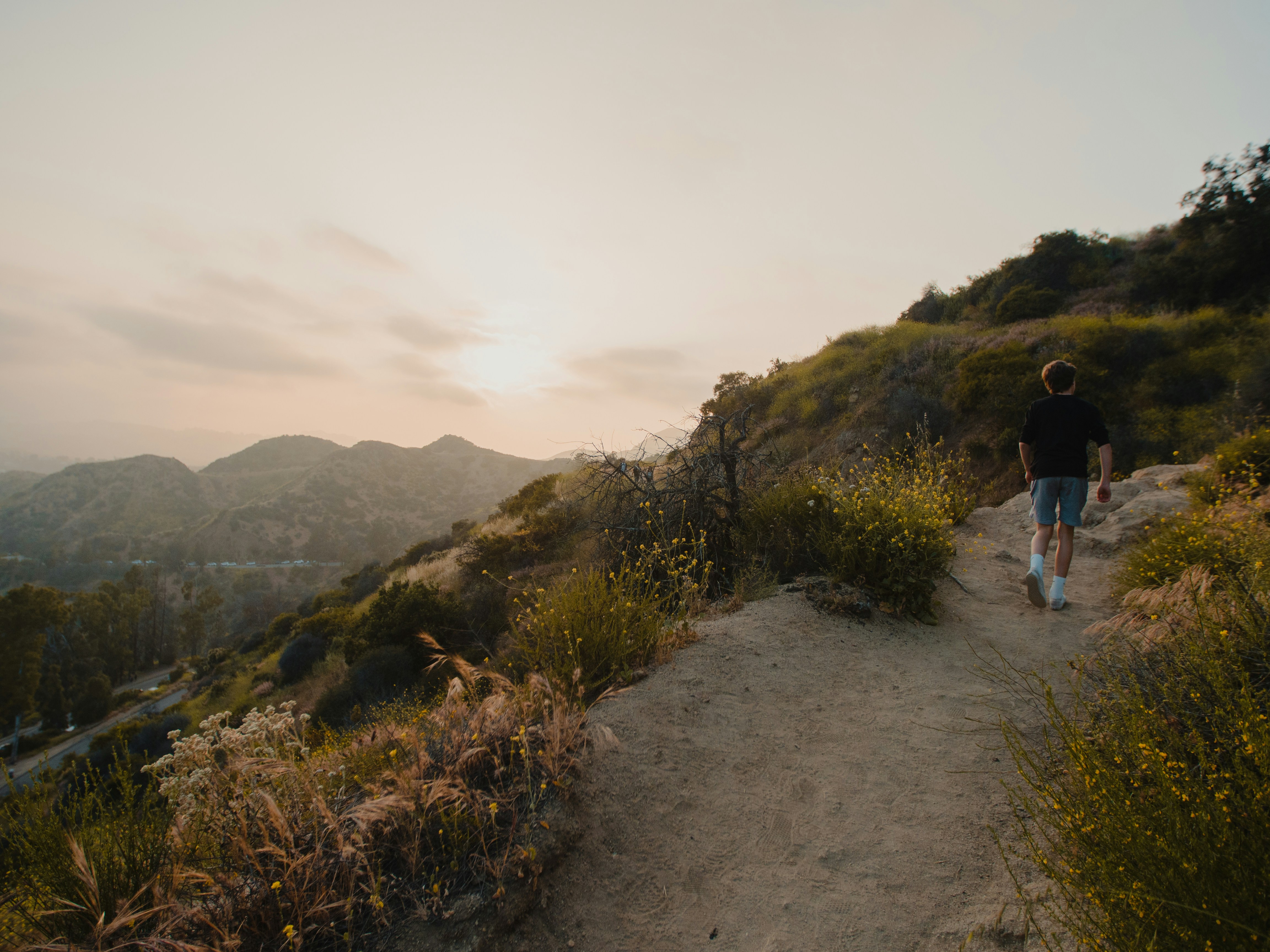 man in black t-shirt and blue denim jeans walking on dirt road during daytime